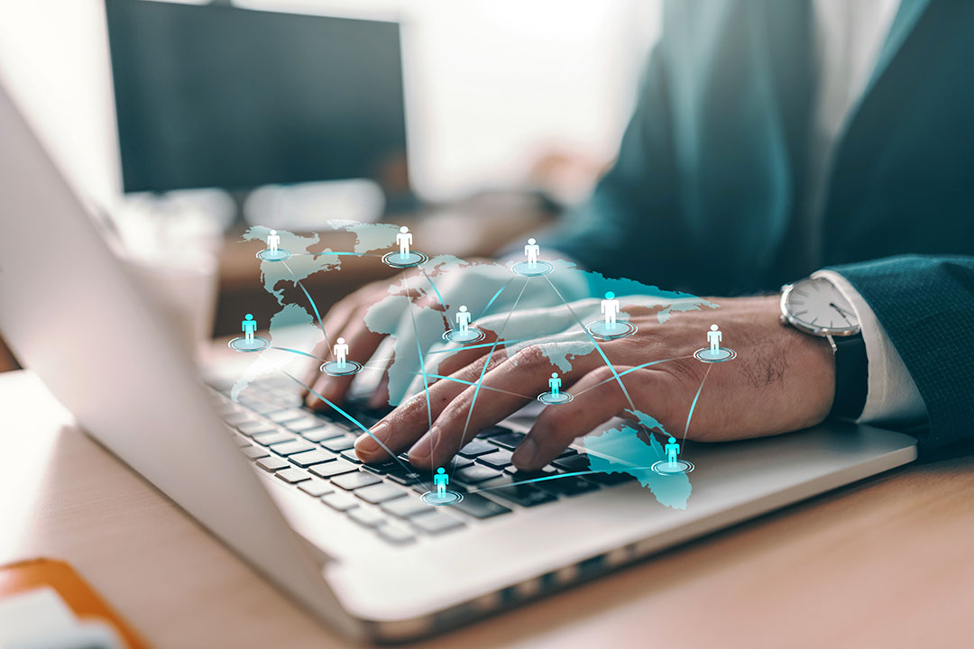 Hände tippen auf einem Laptop, darüber eine Weltkarte mit verbundenen Personensymbolen: Netzwerke und Kooperationen